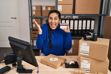 Poster - Young hispanic woman working at small business ecommerce holding credit card celebrating victory with happy smile and winner expression with raised hands