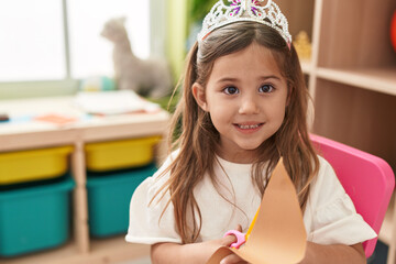 Wall Mural - Adorable blonde girl student wearing princess crown cutting paper at kindergarten