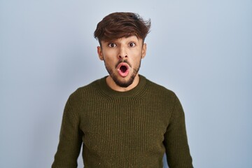 Canvas Print - Arab man with beard standing over blue background afraid and shocked with surprise expression, fear and excited face.