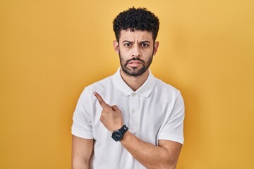 Sticker - Arab man standing over yellow background pointing aside worried and nervous with forefinger, concerned and surprised expression