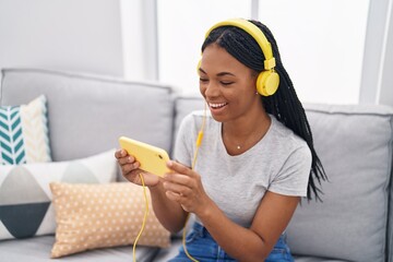 Poster - African american woman watching video on smartphone sitting on sofa at home