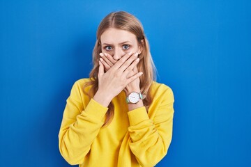 Sticker - Young caucasian woman standing over blue background shocked covering mouth with hands for mistake. secret concept.