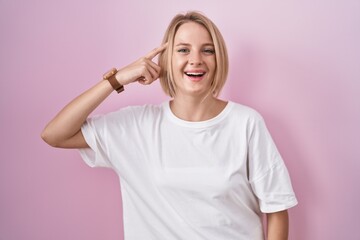 Sticker - Young caucasian woman standing over pink background smiling pointing to head with one finger, great idea or thought, good memory