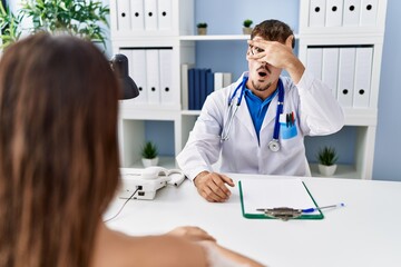 Canvas Print - Young doctor with client at medical clinic peeking in shock covering face and eyes with hand, looking through fingers with embarrassed expression.