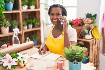 Canvas Print - Middle age african american woman florist talking on smartphone writing on notebook at flower shop