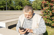 Caucasian senior man sitting on  bench and using cellular at sunny autumnal day in Ukraine