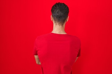 Sticker - Young hispanic man standing over red background standing backwards looking away with crossed arms