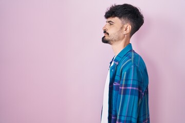 Poster - Young hispanic man with beard standing over pink background looking to side, relax profile pose with natural face with confident smile.