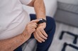 © Krakenimages.com - Middle age grey-haired man touching watch sitting on sofa at home