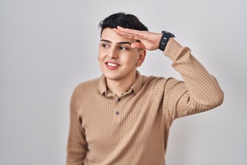 Canvas Print - Non binary person standing over isolated background very happy and smiling looking far away with hand over head. searching concept.