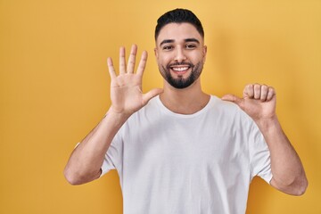 Canvas Print - Young handsome man wearing casual t shirt over yellow background showing and pointing up with fingers number six while smiling confident and happy.