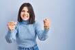 © Krakenimages.com - Young hispanic woman standing over blue background angry and mad raising fists frustrated and furious while shouting with anger. rage and aggressive concept.