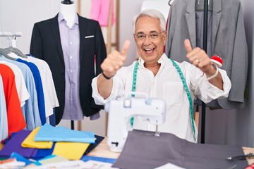 Poster - Middle age man with grey hair dressmaker using sewing machine approving doing positive gesture with hand, thumbs up smiling and happy for success. winner gesture.