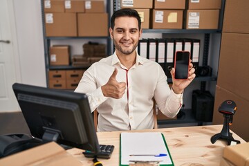 Sticker - Young hispanic man with beard working at small business ecommerce showing smartphone screen smiling happy and positive, thumb up doing excellent and approval sign