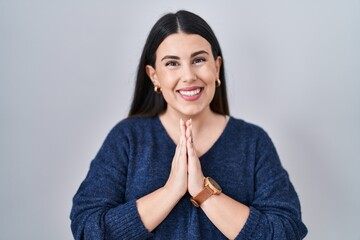 Canvas Print - Young brunette woman standing over isolated background praying with hands together asking for forgiveness smiling confident.