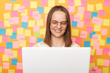 Wall Mural - horizontal shot of satisfied beautiful young adult woman wearing t-shirt posing against yellow paper