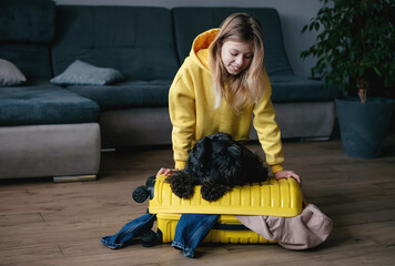 Wall Mural - girl is packing her suitcase. Yellow plastic travel bag. The girl collects clothes for a trip. Journey concept.