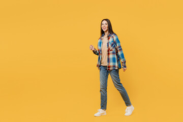 Poster - Full body side view young smiling cheerful caucasian woman wears blue shirt beige t-shirt walk go strolling look camera isolated on plain yellow background studio portrait. People lifestyle concept.