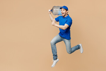 Wall Mural - Full body sideways delivery guy employee man wearing blue cap t-shirt uniform workwear work as dealer courier hold big water bottle jump high isolated on plain light beige background. Service concept.