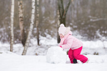Little Girl In Pink Warm Clothes Rolling White Big Snowball At Nature Park. Cute 3 Years Old Toddler Enjoying Cold Winter Day. Side View.