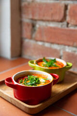 Two portions of shakshuka in red and green baking dishes on a wooden tray, vertical.  Traditional Israeli and Arabic dish shakshuka consisting of eggs poached in a spicy sauce of tomatoes, onion, bell