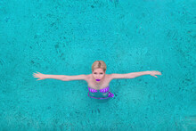 Glamorous Woman In A Swimming Costume Swims In A Pool In Blue Water. View From Above. Hands To The Side.