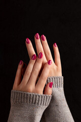 Wall Mural - Female hands in gray knitted sweater with beautiful manicure - viva magenta, pink nails on dark black background. Nail care concept