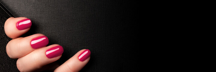 Wall Mural - Female hand with beautiful manicure - viva magenta, pink nails on black leather surface background banner with copy space. Wide panoramic header