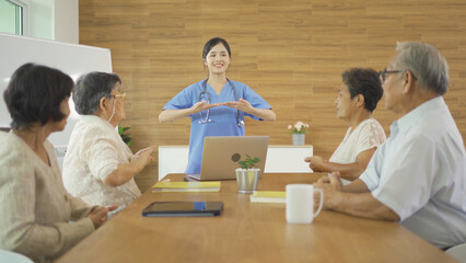 Wall Mural - An Asian nurse talking to a group of old elderly patient or pensioner people smiling, relaxing, having fun together in nursing home. Senior lifestyle activity recreation. Retirement. Health care