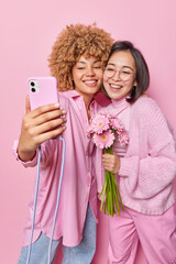 Wall Mural - happy cheerful young women pose together for selfie hold boquet of gerbera flowers smile broadly wea