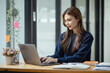 © SOMKID - Happy smiling young asian business woman using laptop sitting at desk in the office, Company worker woman.