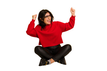 Young indian woman sitting on the floor cut out isolated raising fist after a victory, winner concept.