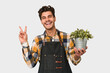 Young caucasian gardener man isolated on white background joyful and carefree showing a peace symbol with fingers.