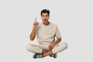 Young caucasian man sitting on the floor isolated on white background having an idea, inspiration concept.