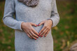 pregnancy, love, family and people concept - close up of pregnant woman making hand heart gesture on her belly