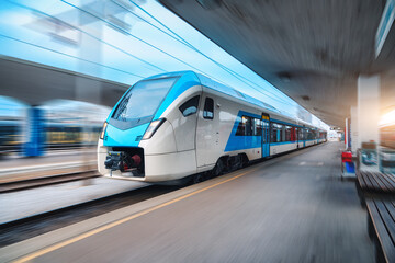 Wall Mural - blue high speed train in motion on the railway station at sunset. fast modern intercity train and bl