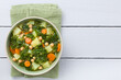 Fresh homemade vegan vegetable soup made of kale, chickpea, carrot, celery, onion and potato, photographed overhead on white wood with copy space on the side (Selective Focus, Focus on the soup)