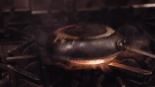 Black Frying Pan Is Placed Upside Down On A Pan With High Flames Coming Out While The Chicken Is Being Cooked. Close Up Panning Shot