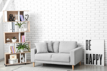 Interior of light living room with grey sofa, shelving unit and poster