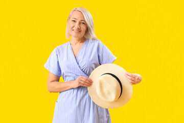 Wall Mural - Stylish blonde mature woman with hat on yellow background