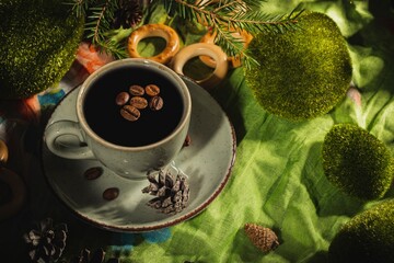 Wall Mural - Still life- a cup of hot coffee and roasted beans. Breakfast mug on a dark green background- table is decorated with sprigs of spruce.