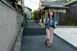© PR Image Factory - full length of Asian Japanese female tourist looking at house buildings with curiosity while walking on a quiet street in residential area in uji shi Kyoto japan