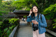 © PR Image Factory - confused asian korean female tourist looking into distance for directions while using navigation app on the phone on the bridge at entrance gate of ujigami jinja in Kyoto japan
