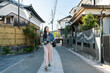 © PR Image Factory - full length of leisure asian Japanese female visitor looking at house buildings while walking on a paved street in residential area of uji city in Kyoto japan