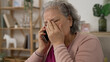© PRPicturesProduction - shoulder shot of a sad asian grandma covering her face in agony on receiving a terrible news on the mobile phone in the living room at home.
