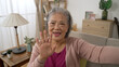 mobile cam view of a happy asian elderly woman waving hand and talking with a smile during a virtual chat with friend in the living room at home