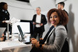 © Pintau Studio - Close-up latin businesswoman looking at camera smiling. Female sitting at desk using computer laptop. Team working during a meeting.