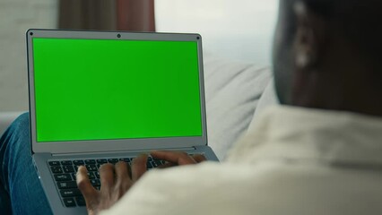 Over shoulder shot african american man businessman programmer freelancer typing on laptop work remote at home on couch looking at green mock-up screen chroma key browsing website make order online