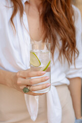 Glass of sparkling water or gin tonik with slices of lime held by a woman