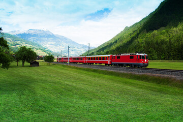 Wall Mural - Red train crossing green valley near Alps
